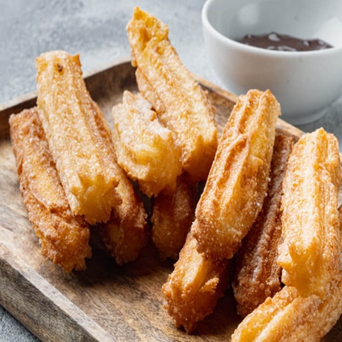 Sugar-dusted churros on a board with a bowl of chocolate dip