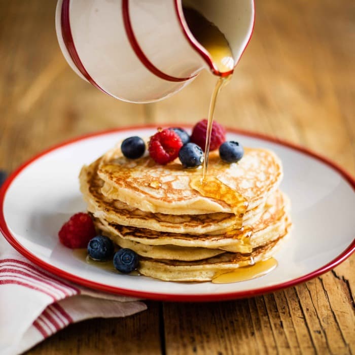 Tall stack of pancakes with berries and syrup being poured over
